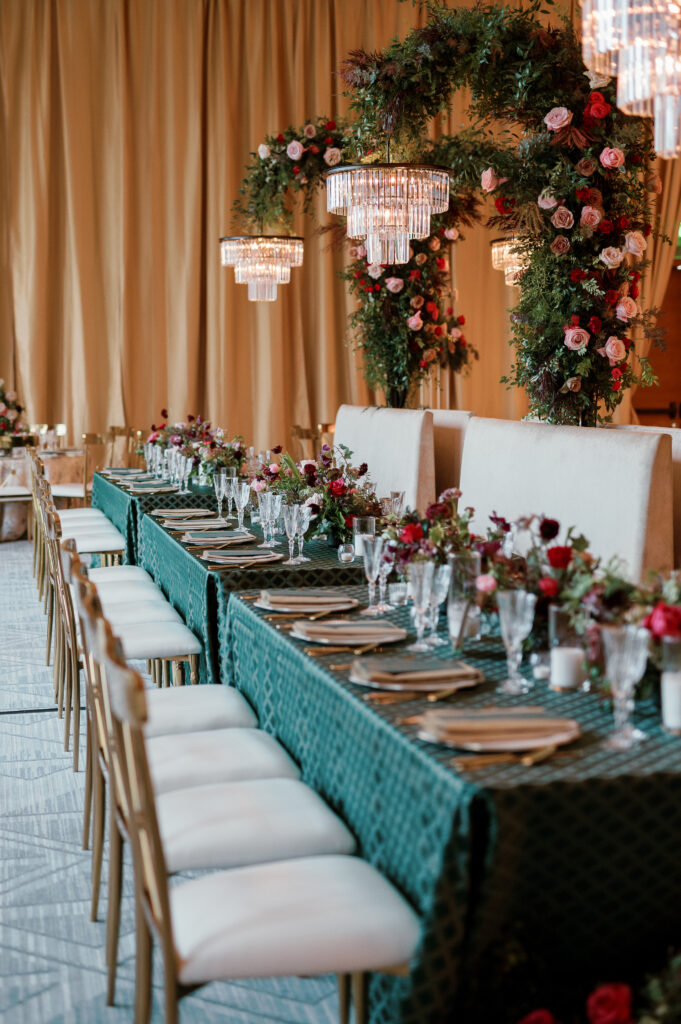 Standing chandeliers covered in lush florals for winter wedding at the Four Seasons. Jewel tone wedding reception florals with reception table floral cascades and table meadows. Winter floral colors in ruby, blush, plum, and magenta. Accent arrangement runners for wedding reception tablescapes. Design by Rosemary & Finch Floral Design.