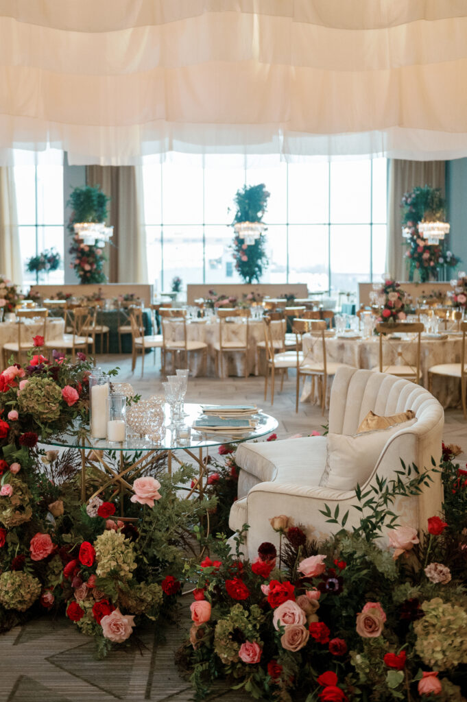 Sweetheart table surrounded by floral meadows in wedding reception. Moody jewel tone wedding reception florals in ruby, blush, plum, and magenta. Winter wedding reception at the Four Seasons. Lush floral moment for wedding sweetheart table. Design by Rosemary & Finch Floral Design. 