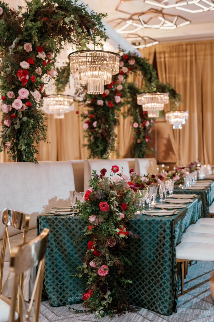 Standing chandeliers covered in lush florals for winter wedding at the Four Seasons. Jewel tone wedding reception florals with reception table floral cascades and table meadows. Winter floral colors in ruby, blush, plum, and magenta. Accent arrangement runners for wedding reception tablescapes. Design by Rosemary & Finch Floral Design.