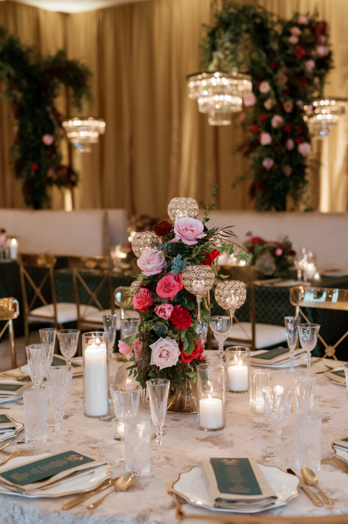 Candelabra with florals surrounding base on wedding tables. Lush florals on crystal candles in for winter wedding reception. Moody jewel tone wedding reception florals in ruby, blush, plum, and magenta. Unique wedding reception centerpieces. Wedding reception in Downtown Nashville at the Four Seasons. Design by Rosemary & Finch Floral Design.