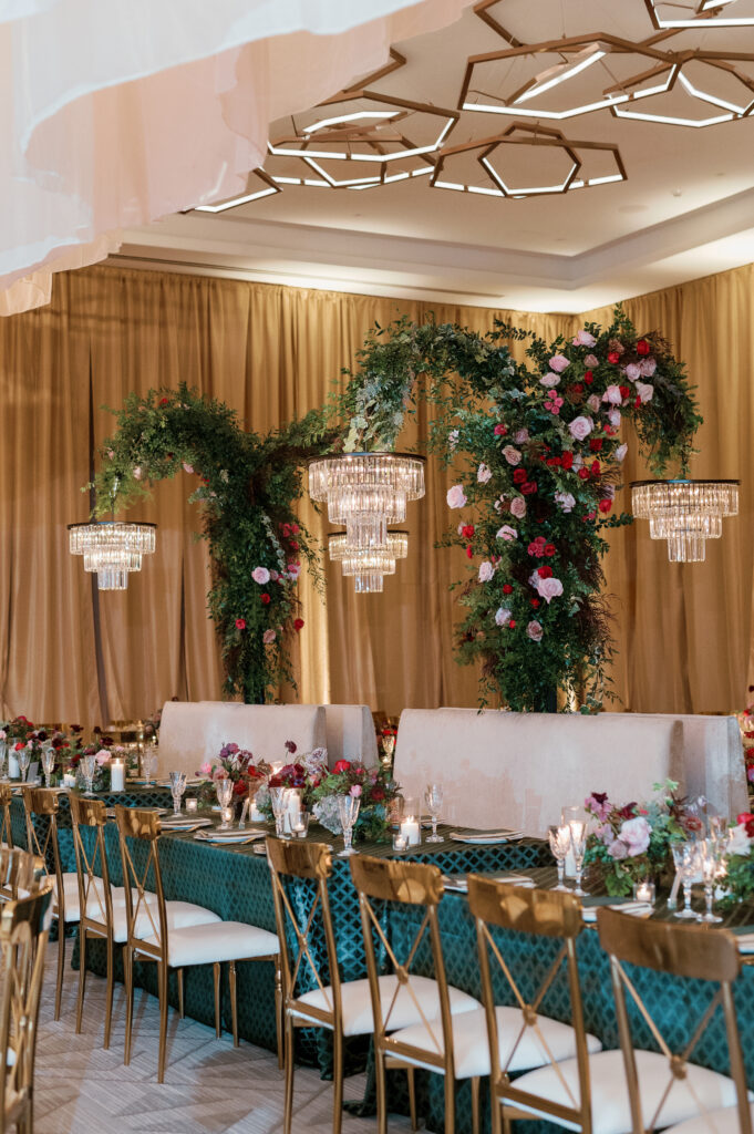 Standing chandeliers covered in lush florals for winter wedding at the Four Seasons. Jewel tone wedding reception florals with reception table floral cascades and table meadows. Winter floral colors in ruby, blush, plum, and magenta. Accent arrangement runners for wedding reception tablescapes. Design by Rosemary & Finch Floral Design.