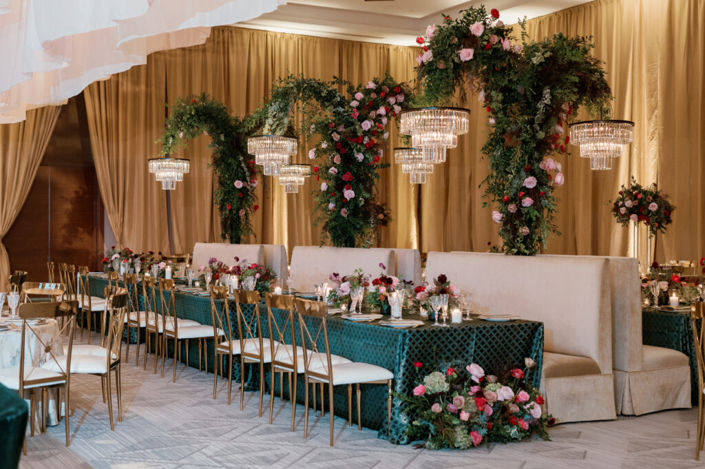 Standing chandeliers covered in lush florals for winter wedding at the Four Seasons. Jewel tone wedding reception florals with reception table floral cascades and table meadows. Winter floral colors in ruby, blush, plum, and magenta. Accent arrangement runners for wedding reception tablescapes. Design by Rosemary & Finch Floral Design.