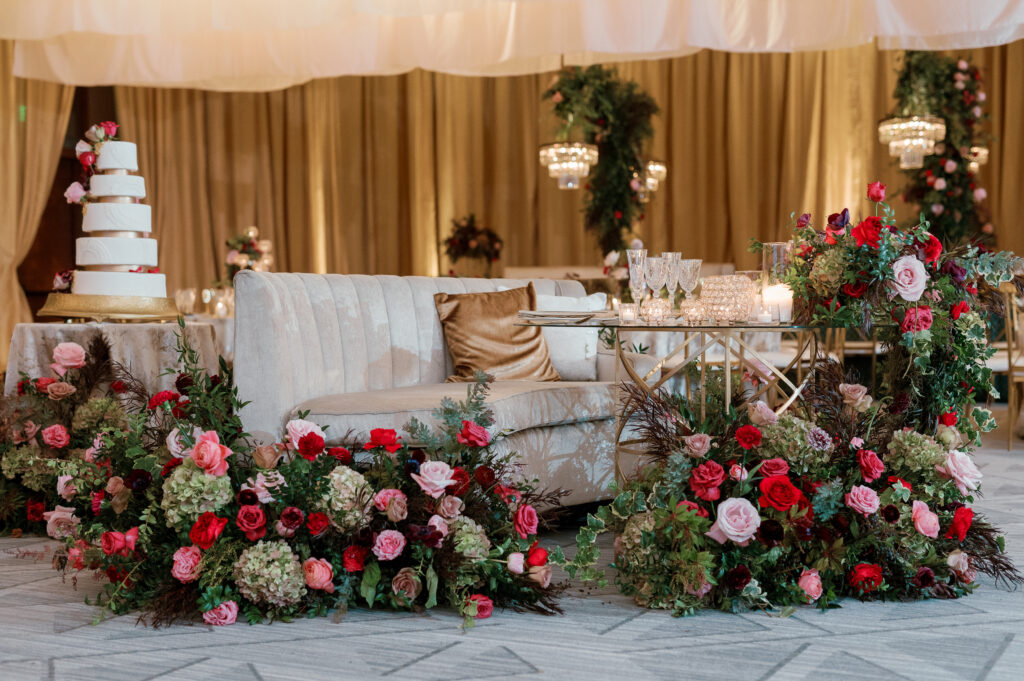 Sweetheart table surrounded by floral meadows in wedding reception. Moody jewel tone wedding reception florals in ruby, blush, plum, and magenta. Winter wedding reception at the Four Seasons. Lush floral moment for wedding sweetheart table. Design by Rosemary & Finch Floral Design. 