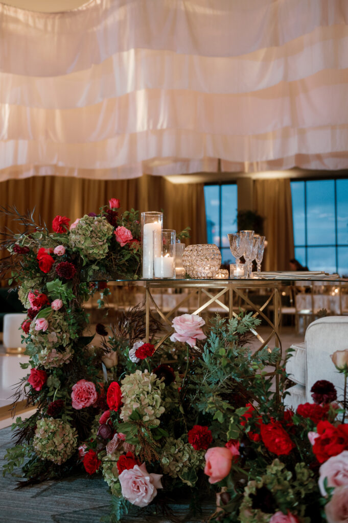 Sweetheart table surrounded by floral meadows in wedding reception. Moody jewel tone wedding reception florals in ruby, blush, plum, and magenta. Winter wedding reception at the Four Seasons. Lush floral moment for wedding sweetheart table. Design by Rosemary & Finch Floral Design. 