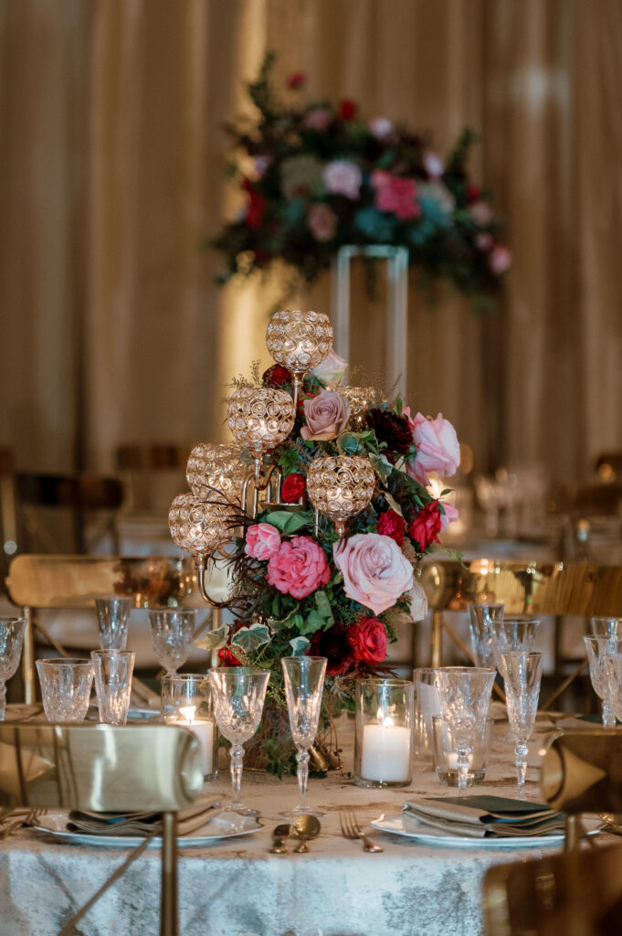 Candelabra with florals surrounding base on wedding tables. Lush florals on crystal candles in for winter wedding reception. Moody jewel tone wedding reception florals in ruby, blush, plum, and magenta. Unique wedding reception centerpieces. Wedding reception in Downtown Nashville at the Four Seasons. Design by Rosemary & Finch Floral Design.