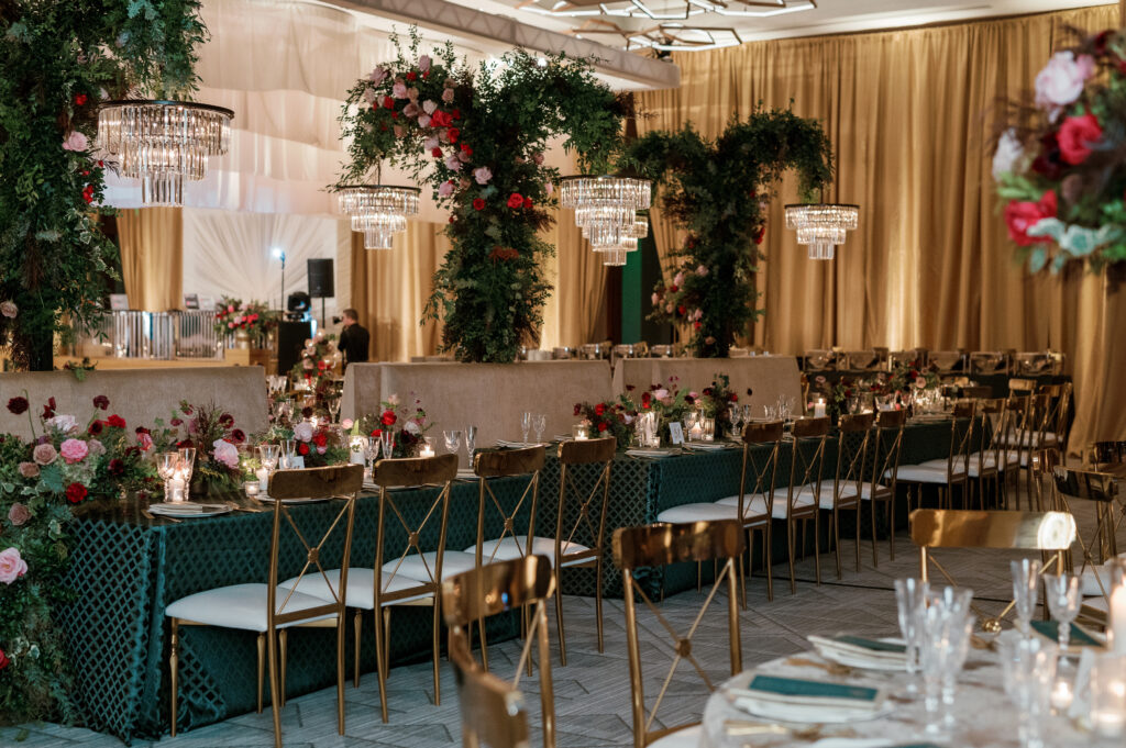 Standing chandeliers covered in lush florals for winter wedding at the Four Seasons. Jewel tone wedding reception florals with reception table floral cascades and table meadows. Winter floral colors in ruby, blush, plum, and magenta. Accent arrangement runners for wedding reception tablescapes. Design by Rosemary & Finch Floral Design.