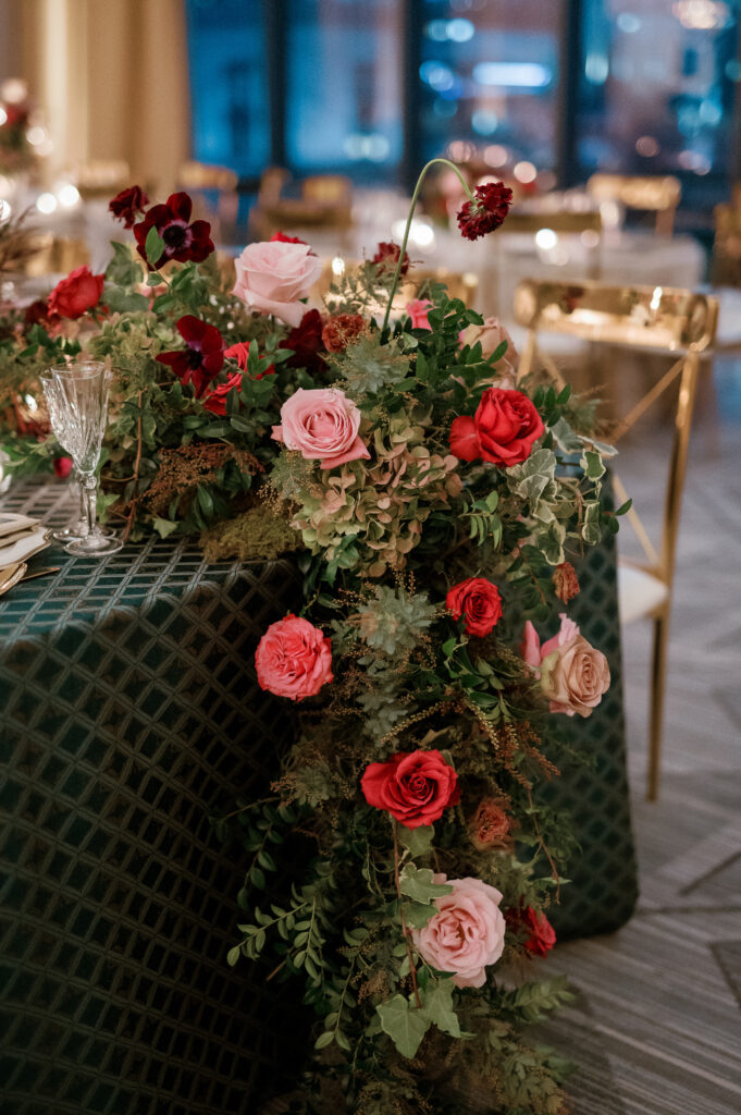 Standing chandeliers covered in lush florals for winter wedding at the Four Seasons. Jewel tone wedding reception florals with reception table floral cascades and table meadows. Winter floral colors in ruby, blush, plum, and magenta. Accent arrangement runners for wedding reception tablescapes. Design by Rosemary & Finch Floral Design.