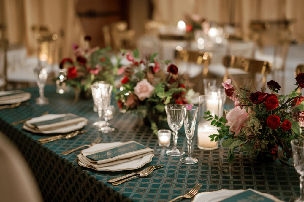 Jewel tone wedding reception florals with reception table floral cascades and table meadows. Winter floral colors in ruby, blush, plum, and magenta. Accent arrangement runners for wedding reception tablescapes. Design by Rosemary & Finch Floral Design.