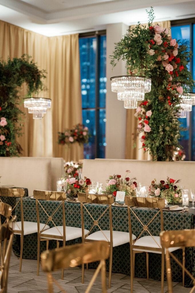 Standing chandeliers covered in lush florals for winter wedding at the Four Seasons. Jewel tone wedding reception florals with reception table floral cascades and table meadows. Winter floral colors in ruby, blush, plum, and magenta. Accent arrangement runners for wedding reception tablescapes. Design by Rosemary & Finch Floral Design.