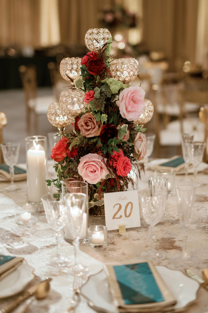 Candelabra with florals surrounding base on wedding tables. Lush florals on crystal candles in for winter wedding reception. Moody jewel tone wedding reception florals in ruby, blush, plum, and magenta. Unique wedding reception centerpieces. Wedding reception in Downtown Nashville at the Four Seasons. Design by Rosemary & Finch Floral Design.