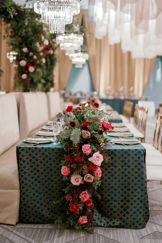 Standing chandeliers covered in lush florals for winter wedding at the Four Seasons. Jewel tone wedding reception florals with reception table floral cascades and table meadows. Winter floral colors in ruby, blush, plum, and magenta. Accent arrangement runners for wedding reception tablescapes. Design by Rosemary & Finch Floral Design.