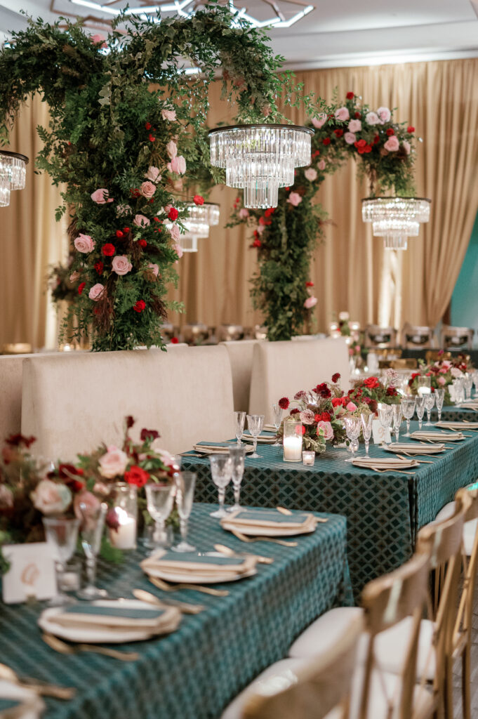 Standing chandeliers covered in lush florals for winter wedding at the Four Seasons. Jewel tone wedding reception florals with reception table floral cascades and table meadows. Winter floral colors in ruby, blush, plum, and magenta. Accent arrangement runners for wedding reception tablescapes. Design by Rosemary & Finch Floral Design.