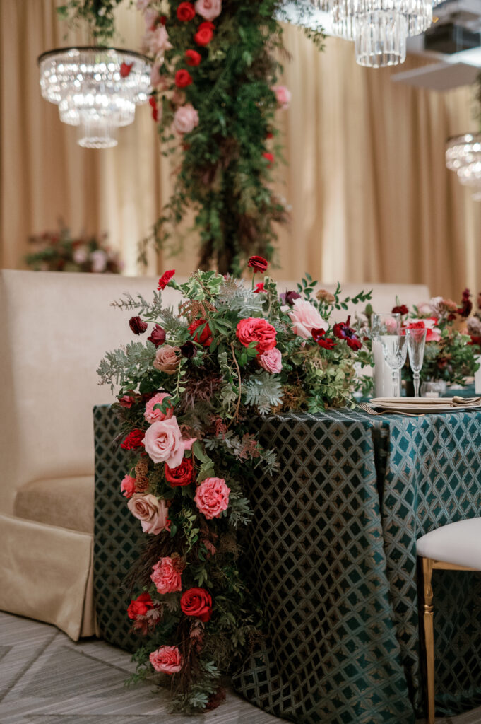 Standing chandeliers covered in lush florals for winter wedding at the Four Seasons. Jewel tone wedding reception florals with reception table floral cascades and table meadows. Winter floral colors in ruby, blush, plum, and magenta. Accent arrangement runners for wedding reception tablescapes. Design by Rosemary & Finch Floral Design.