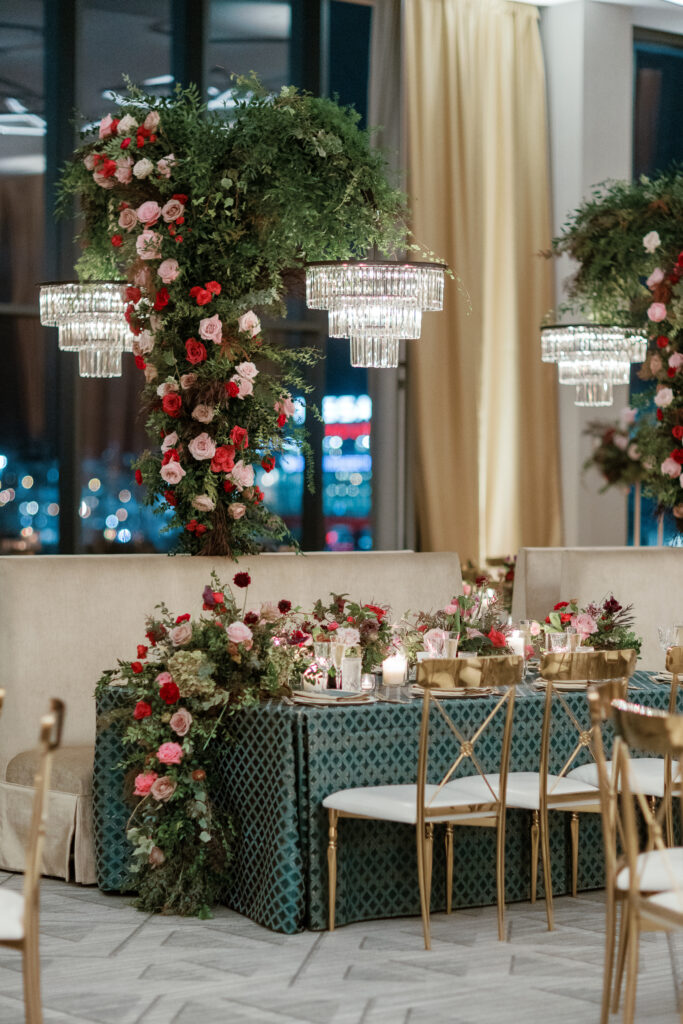 Standing chandeliers covered in lush florals for winter wedding at the Four Seasons. Jewel tone wedding reception florals with reception table floral cascades and table meadows. Winter floral colors in ruby, blush, plum, and magenta. Accent arrangement runners for wedding reception tablescapes. Design by Rosemary & Finch Floral Design.