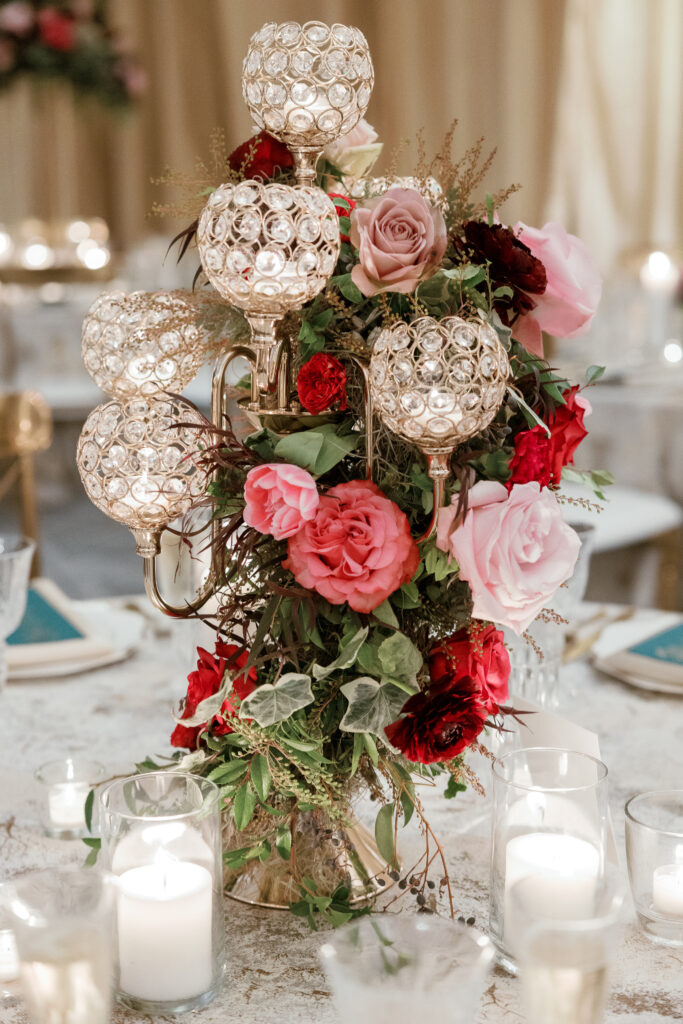 Candelabra with florals surrounding base on wedding tables. Lush florals on crystal candles in for winter wedding reception. Moody jewel tone wedding reception florals in ruby, blush, plum, and magenta. Unique wedding reception centerpieces. Wedding reception in Downtown Nashville at the Four Seasons. Design by Rosemary & Finch Floral Design.