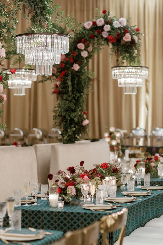 Standing chandeliers covered in lush florals for winter wedding at the Four Seasons. Jewel tone wedding reception florals with reception table floral cascades and table meadows. Winter floral colors in ruby, blush, plum, and magenta. Accent arrangement runners for wedding reception tablescapes. Design by Rosemary & Finch Floral Design.