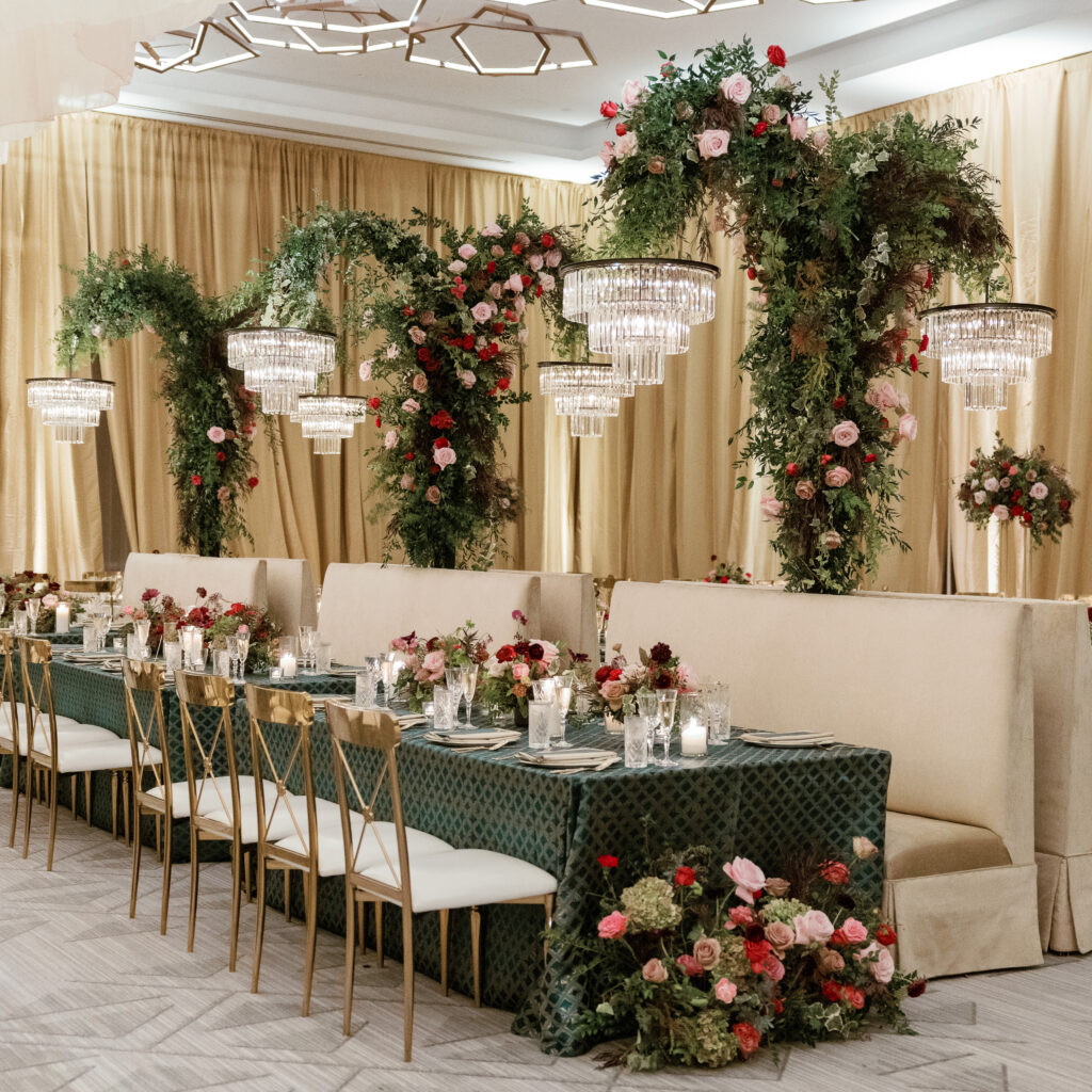 Standing chandeliers covered in lush florals for winter wedding at the Four Seasons. Jewel tone wedding reception florals with reception table floral cascades and table meadows. Winter floral colors in ruby, blush, plum, and magenta. Accent arrangement runners for wedding reception tablescapes. Design by Rosemary & Finch Floral Design.