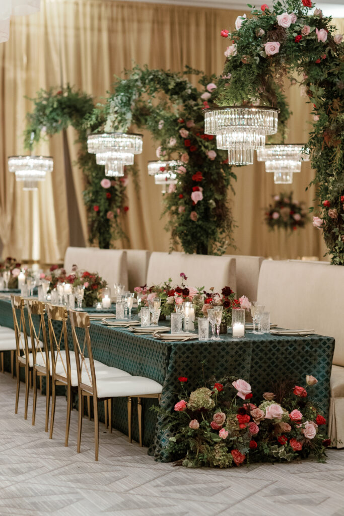 Standing chandeliers covered in lush florals for winter wedding at the Four Seasons. Jewel tone wedding reception florals with reception table floral cascades and table meadows. Winter floral colors in ruby, blush, plum, and magenta. Accent arrangement runners for wedding reception tablescapes. Design by Rosemary & Finch Floral Design.