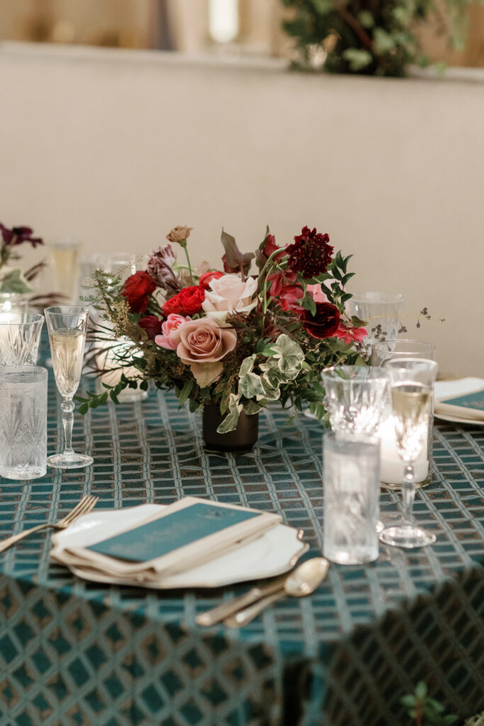 Jewel tone wedding reception florals with reception table floral cascades and table meadows. Winter floral colors in ruby, blush, plum, and magenta. Accent arrangement runners for wedding reception tablescapes. Design by Rosemary & Finch Floral Design.