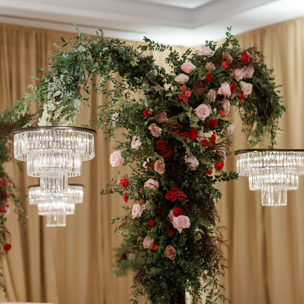 Standing chandeliers covered in lush florals for winter wedding at the Four Seasons. Jewel tone wedding reception florals with reception table floral cascades and table meadows. Winter floral colors in ruby, blush, plum, and magenta. Accent arrangement runners for wedding reception tablescapes. Design by Rosemary & Finch Floral Design.