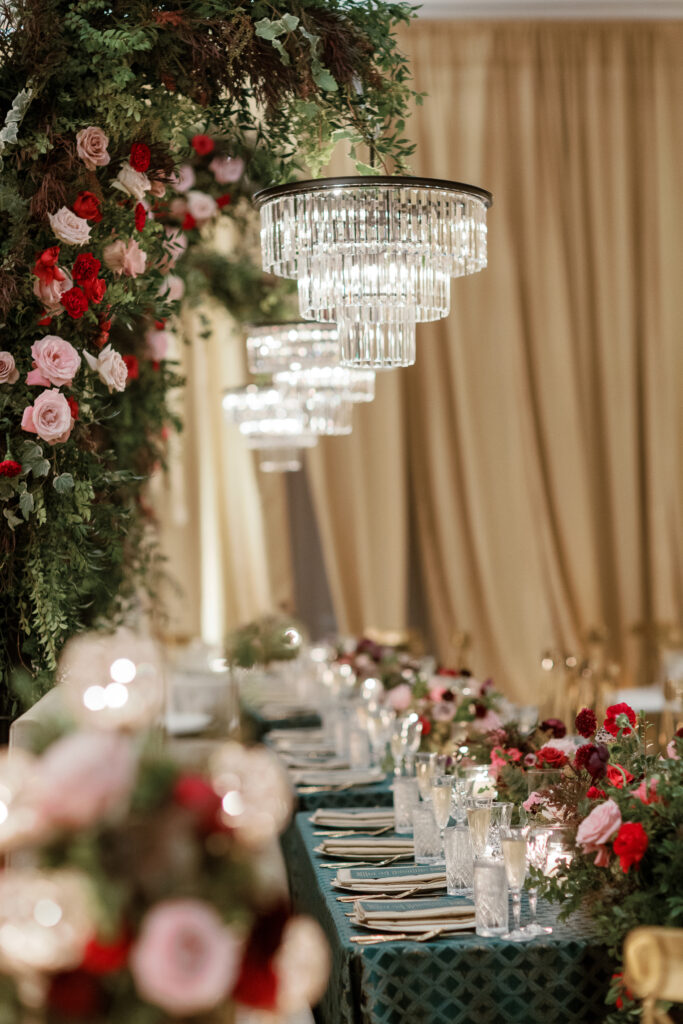 Standing chandeliers covered in lush florals for winter wedding at the Four Seasons. Jewel tone wedding reception florals with reception table floral cascades and table meadows. Winter floral colors in ruby, blush, plum, and magenta. Accent arrangement runners for wedding reception tablescapes. Design by Rosemary & Finch Floral Design.