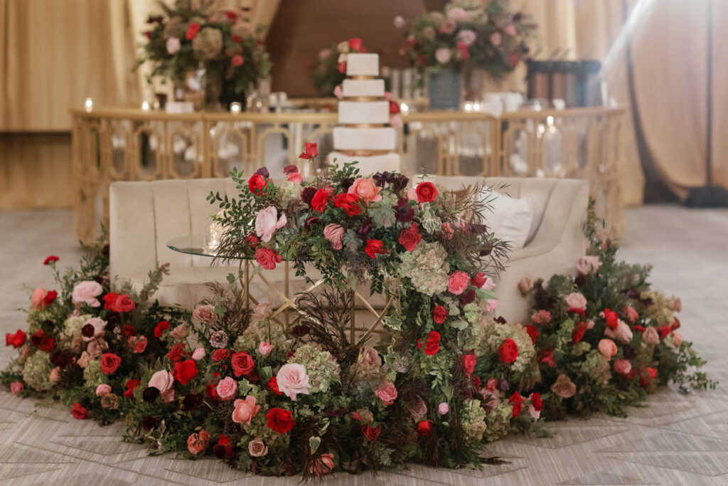 Sweetheart table surrounded by floral meadows in wedding reception. Moody jewel tone wedding reception florals in ruby, blush, plum, and magenta. Winter wedding reception at the Four Seasons. Lush floral moment for wedding sweetheart table. Design by Rosemary & Finch Floral Design. 