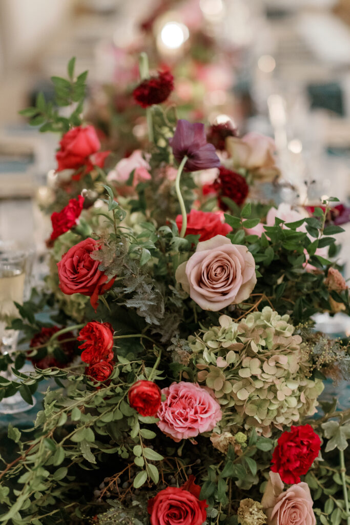 Jewel tone wedding reception florals with reception table floral cascades and table meadows. Winter floral colors in ruby, blush, plum, and magenta. Accent arrangement runners for wedding reception tablescapes. Design by Rosemary & Finch Floral Design.