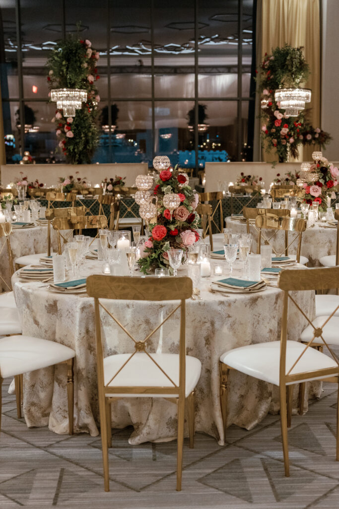 Candelabra with florals surrounding base on wedding tables. Lush florals on crystal candles in for winter wedding reception. Moody jewel tone wedding reception florals in ruby, blush, plum, and magenta. Unique wedding reception centerpieces. Wedding reception in Downtown Nashville at the Four Seasons. Design by Rosemary & Finch Floral Design.