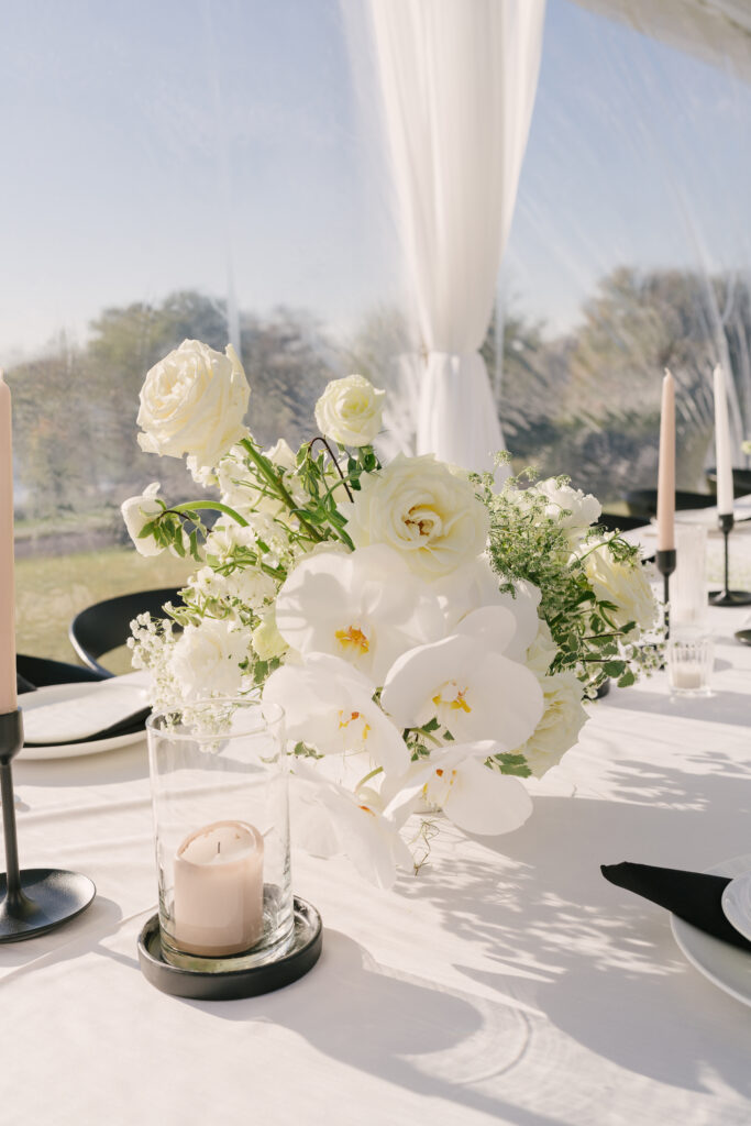 Modern floral centerpieces for fall wedding reception. All white wedding florals with modern black finishes. Timeless flower colors of white, taupe, and green. Neutral candles with modern black candlesticks and trays. White roses, babies’ breath, anthurium, and orchids. Private estate wedding in the Nashville fall. Design by Rosemary & Finch Floral Design.