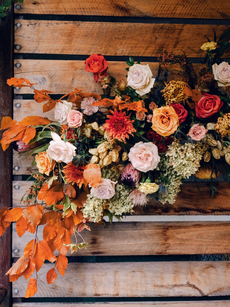 Wedding rehearsal dinner florals for fall wedding. Checkmate themed rehearsal dinner with plaid details and fall florals. Fall floral colors in rust, burgundy, sage, cream, and copper. Fall growing floral installation for rehearsal dinner. Floral design for wedding week events in Nashville, TN. Design by Rosemary & Finch Floral Design.  