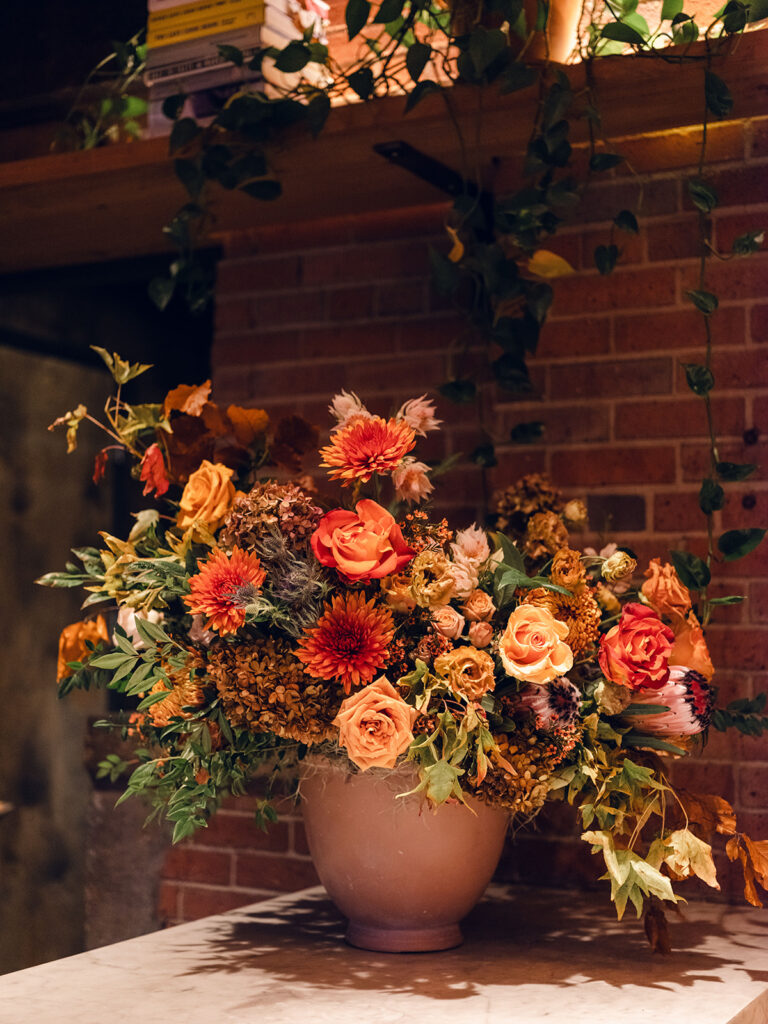 Wedding rehearsal dinner florals for fall wedding. Checkmate themed rehearsal dinner with plaid details and fall florals. Fall floral colors in rust, burgundy, sage, cream, and copper. Fall garden urn statement arrangement on bar. Floral design for wedding week events in Nashville, TN. Design by Rosemary & Finch Floral Design.  