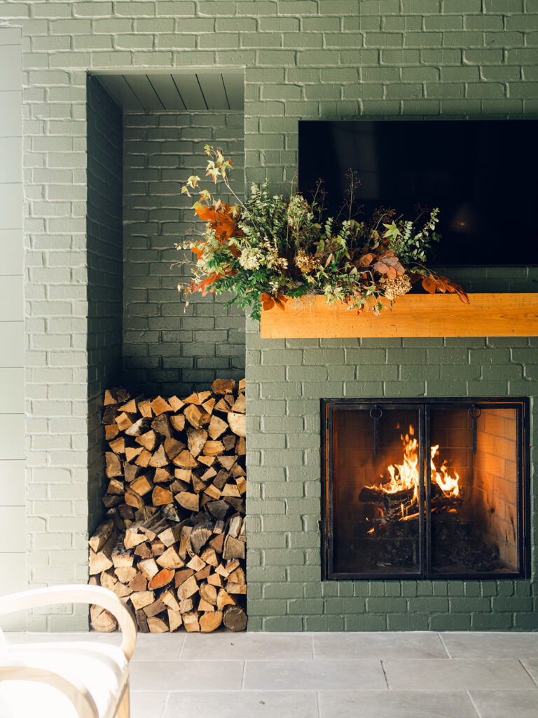 Fireplace fall floral installation for bridesmaids’ luncheon. Outdoor fireplace event décor with fall foliage and green painted brick. Fall event décor with fall foliage and florals in cream, copper, rust, and natural greens. Design by Rosemary & Finch Floral & Finch. 