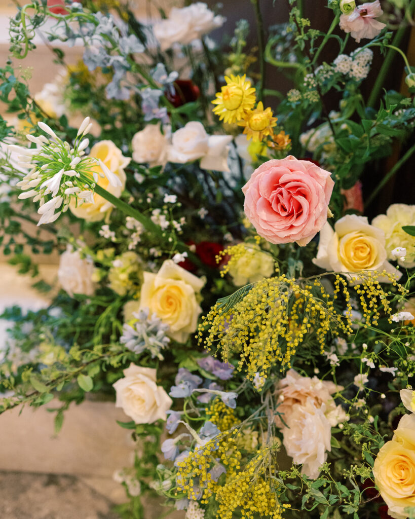 Garden-inspired floral installation on winding staircase. Flowers consisting of soft and vibrant hues, including shades of pink, peach, yellow, cream, and touches of burgundy, adding depth and interest. Winter wedding in downtown Nashville. Unique ceremony entrance for winter wedding. Design by Rosemary & Finch Floral Design. 