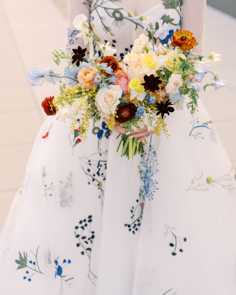 This bridal bouquet features a stunning mix of flowers in a pastel color palette, creating an elegant and romantic look. The combination of soft pastels with darker accents provides a beautiful contrast, while the mix of shapes and textures adds visual interest and depth. Bridesmaids’ bouquets accenting bridal bouquet. Winter wedding in downtown Nashville. Design by Rosemary & Finch Floral Design. 