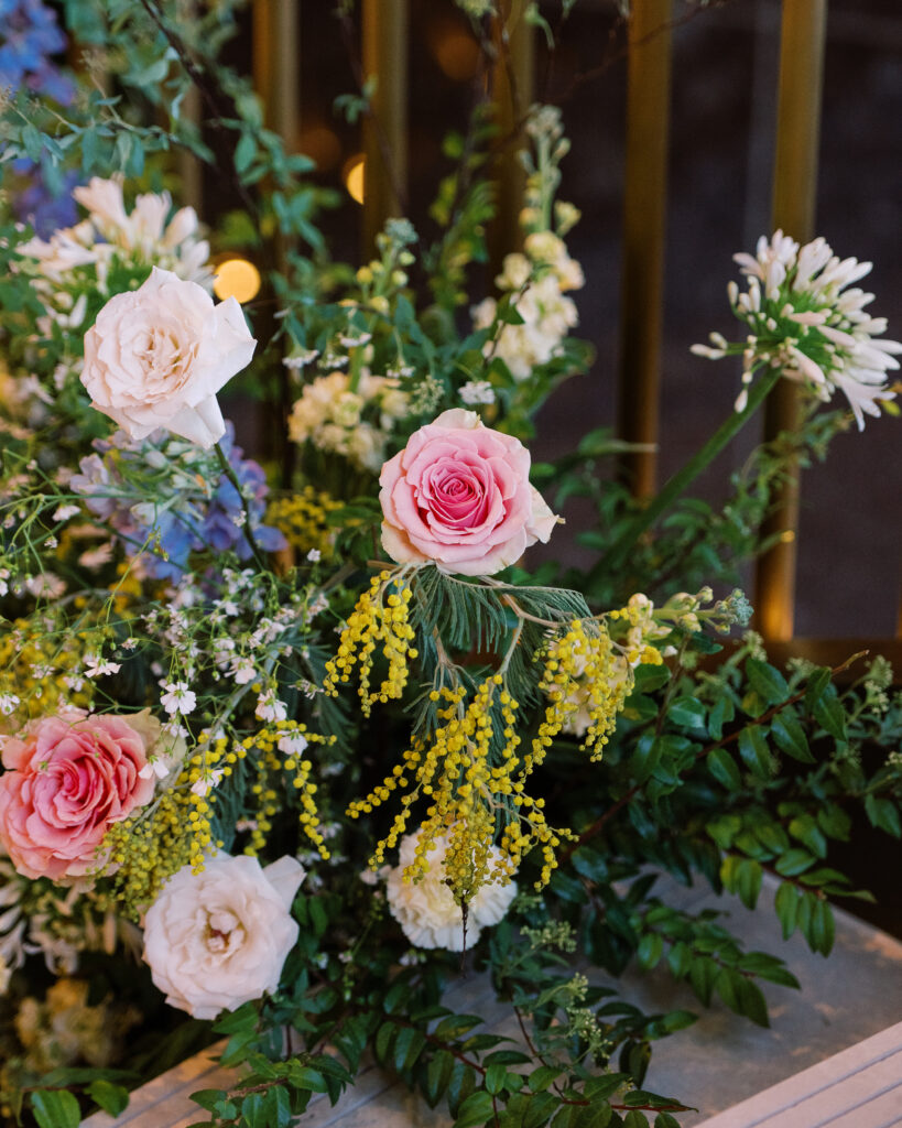 Garden-inspired floral installation on winding staircase. Flowers consisting of soft and vibrant hues, including shades of pink, peach, yellow, cream, and touches of burgundy, adding depth and interest. Winter wedding in downtown Nashville. Unique ceremony entrance for winter wedding. Design by Rosemary & Finch Floral Design. 