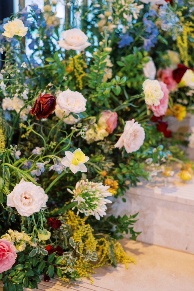 Garden-inspired floral installation on winding staircase. Flowers consisting of soft and vibrant hues, including shades of pink, peach, yellow, cream, and touches of burgundy, adding depth and interest. Winter wedding in downtown Nashville. Unique ceremony entrance for winter wedding. Design by Rosemary & Finch Floral Design. 