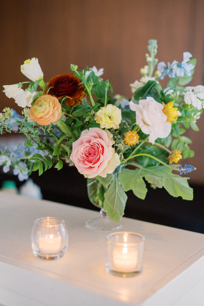 Elegant cocktail hour floral arrangements in clear glass vases. Flowers consisting of soft and vibrant hues, including shades of pink, peach, yellow, cream, and touches of burgundy, adding depth and interest. Winter wedding in downtown Nashville. Design by Rosemary & Finch Floral Design.