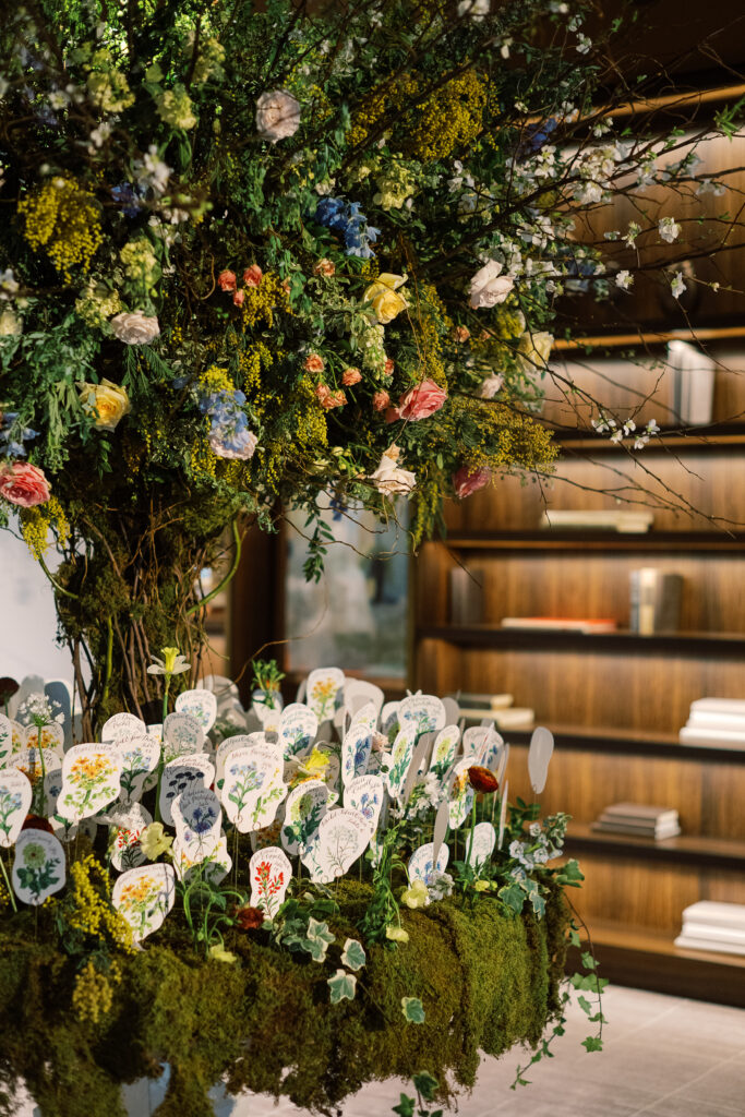 Tree escort display with hand illustrated escort cards in flower meadows. Mossy floral meadows hold escort cards for winter wedding reception. Unique wedding color palette consisting of reds, butter yellows, soft blue, and rich burgundy. Design by Rosemary & Finch Floral Design.