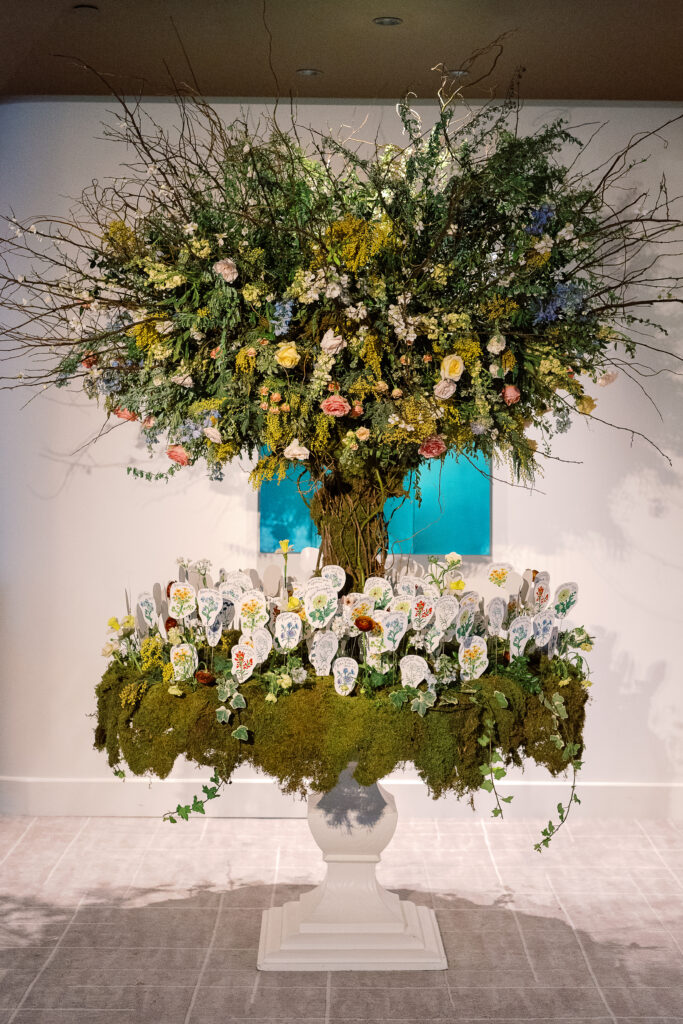 Tree escort display with hand illustrated escort cards in flower meadows. Mossy floral meadows hold escort cards for winter wedding reception. Unique wedding color palette consisting of reds, butter yellows, soft blue, and rich burgundy. Design by Rosemary & Finch Floral Design.