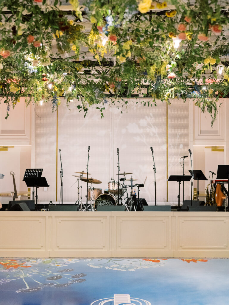 Airy garden-inspired floral installation hanging over wedding reception dance floor. Vining floral garden inspired installation gives interest to the dance floor of this winter wedding in downtown Nashville. Mixed flowers in soft pastel colors, including yellows, whites, and some darker tones like red and burgundy. Design by Rosemary & Finch Floral Design in Nashville, TN.