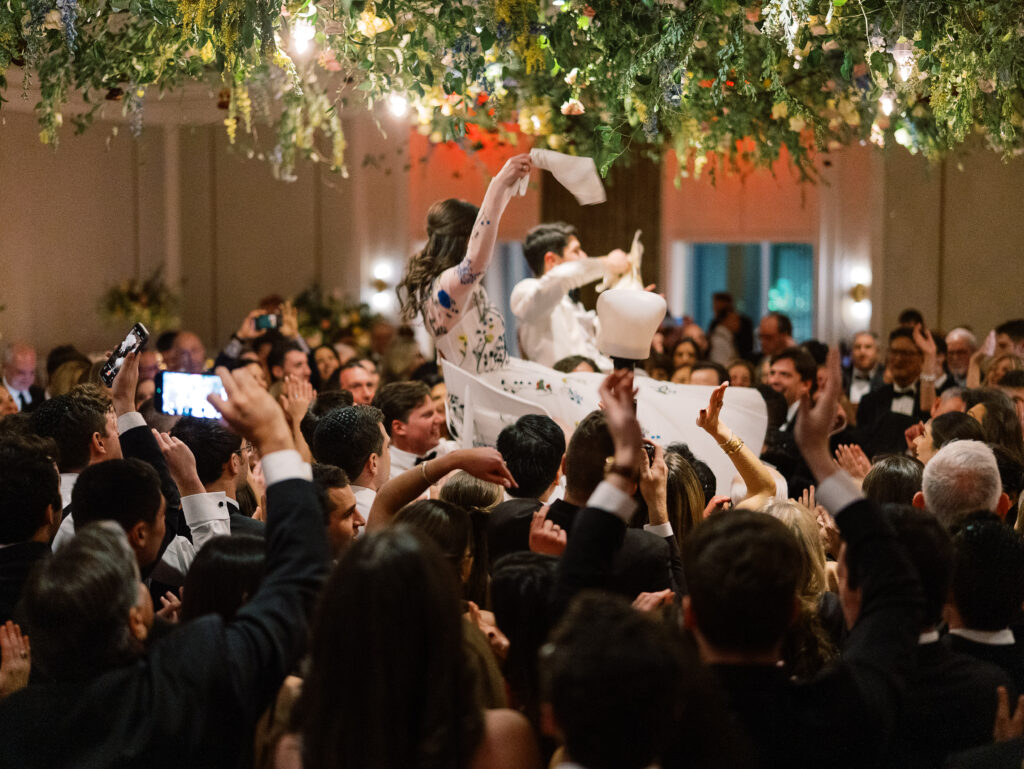 Airy garden-inspired floral installation hanging over wedding reception dance floor. Vining floral garden inspired installation gives interest to the dance floor of this winter wedding in downtown Nashville. Mixed flowers in soft pastel colors, including yellows, whites, and some darker tones like red and burgundy. Design by Rosemary & Finch Floral Design in Nashville, TN.