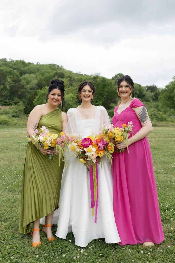 Vibrant and colorful bridal bouquet with flowers that includes lush, fully bloomed peonies in rich magenta, complemented by bright orange and yellow poppies. Summer bridal and bridesmaids’ bouquet with unique and bold spring colors. Whimsical wedding floral with statement making colors. Design by Rosemary & Finch Floral Design. 