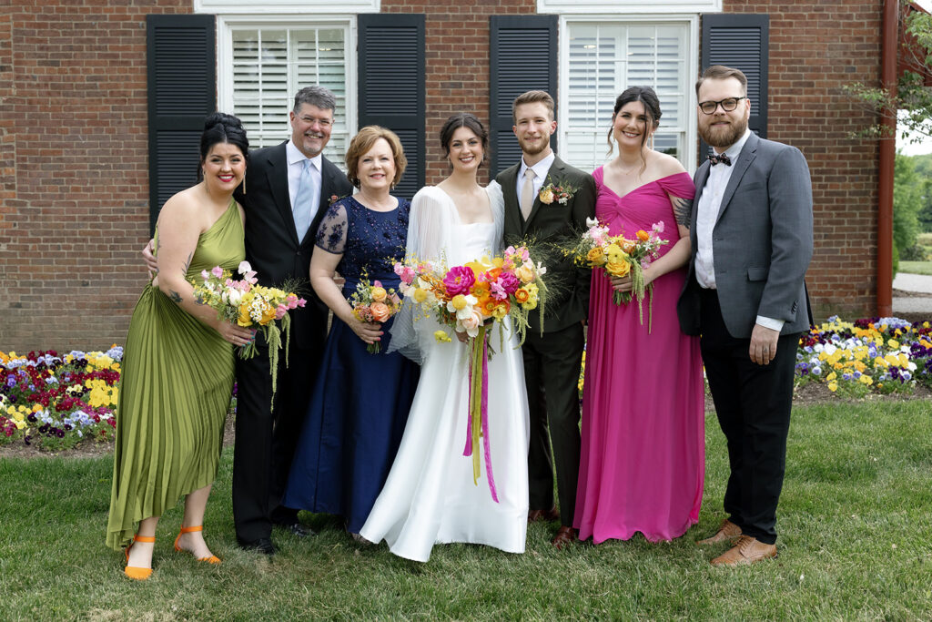 Vibrant and colorful bridal bouquet with flowers that includes lush, fully bloomed peonies in rich magenta, complemented by bright orange and yellow poppies. Summer bridal and bridesmaids’ bouquet with unique and bold spring colors. Whimsical wedding floral with statement making colors. Design by Rosemary & Finch Floral Design. 