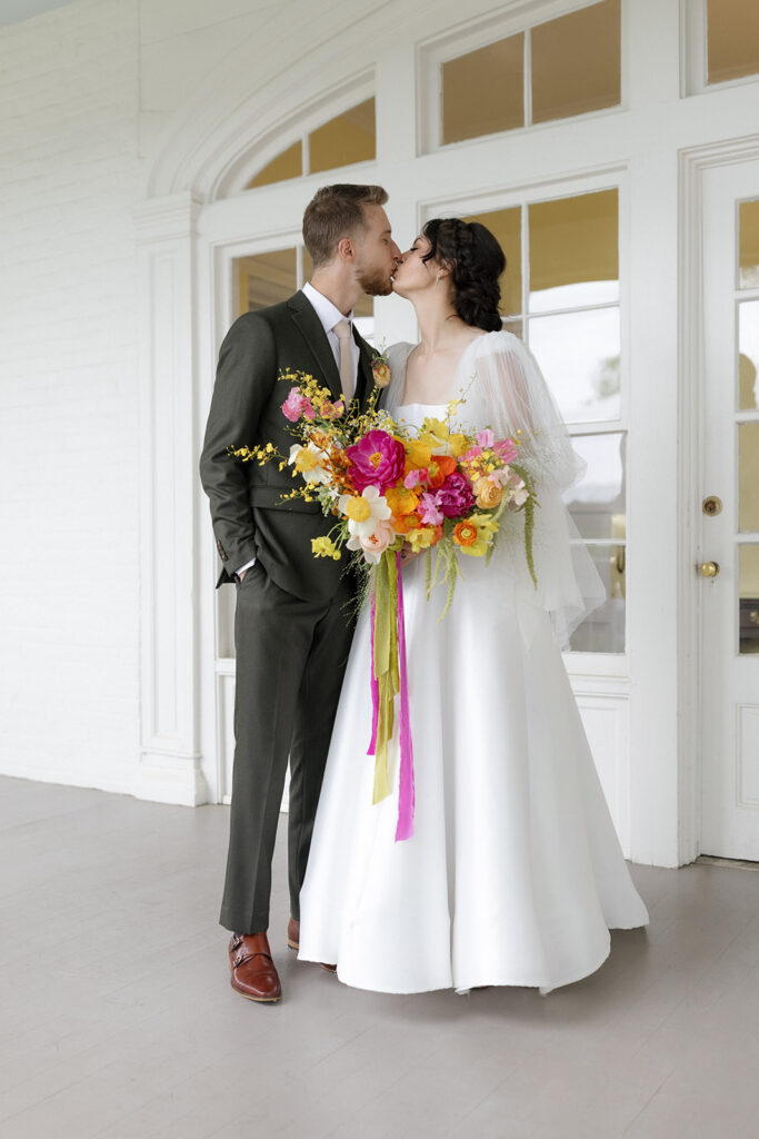 Vibrant and colorful bridal bouquet with flowers that includes lush, fully bloomed peonies in rich magenta, complemented by bright orange and yellow poppies. Summer bridal and bridesmaids’ bouquet with unique and bold spring colors. Whimsical wedding floral with statement making colors. Design by Rosemary & Finch Floral Design. 