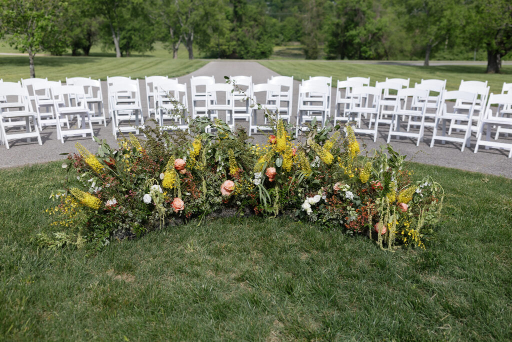 Floral ground meadows for spring wedding ceremony. Unique circle ceremony for outdoor Tennessee wedding. Ceremony floral installation includes a variety of greenery and flowers, with dominant hues of yellow and orange, accented by soft pink and white roses. Unique vibrant spring florals. Design by Rosemary & Finch Floral Design in Nashville, TN.