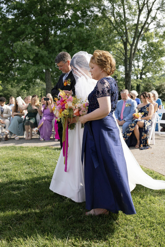 Vibrant and colorful bridal bouquet with flowers that includes lush, fully bloomed peonies in rich magenta, complemented by bright orange and yellow poppies. Summer bridal and bridesmaids’ bouquet with unique and bold spring colors. Whimsical wedding floral with statement making colors. Design by Rosemary & Finch Floral Design. 