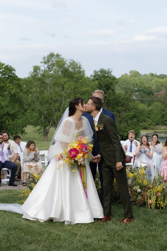 Floral ground meadows for spring wedding ceremony. Unique circle ceremony for outdoor Tennessee wedding. Ceremony floral installation includes a variety of greenery and flowers, with dominant hues of yellow and orange, accented by soft pink and white roses. Unique vibrant spring florals. Design by Rosemary & Finch Floral Design in Nashville, TN.