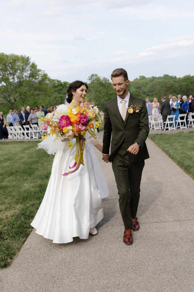 Vibrant and colorful bridal bouquet with flowers that includes lush, fully bloomed peonies in rich magenta, complemented by bright orange and yellow poppies. Summer bridal and bridesmaids’ bouquet with unique and bold spring colors. Whimsical wedding floral with statement making colors. Design by Rosemary & Finch Floral Design. 