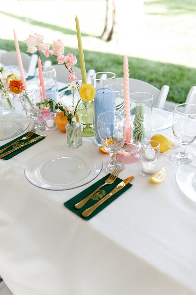 Spring floral centerpieces in bright, cheerful colors, featuring pink peonies, white roses, and wildflowers in orange and yellow. Styled citrus fruits, such as oranges, lemons, limes, and grapefruits for wedding reception tables. Spring wedding with vibrant and unique floral design. Colored glass candle sticks and spiral tapers add unique candle design. Design by Rosemary & Finch Floral Design in Nashville, TN. 