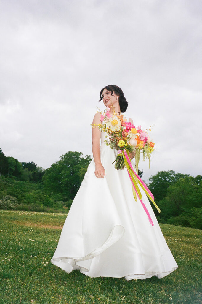 Vibrant and colorful bridal bouquet with flowers that includes lush, fully bloomed peonies in rich magenta, complemented by bright orange and yellow poppies. Summer bridal and bridesmaids’ bouquet with unique and bold spring colors. Whimsical wedding floral with statement making colors. Design by Rosemary & Finch Floral Design. 